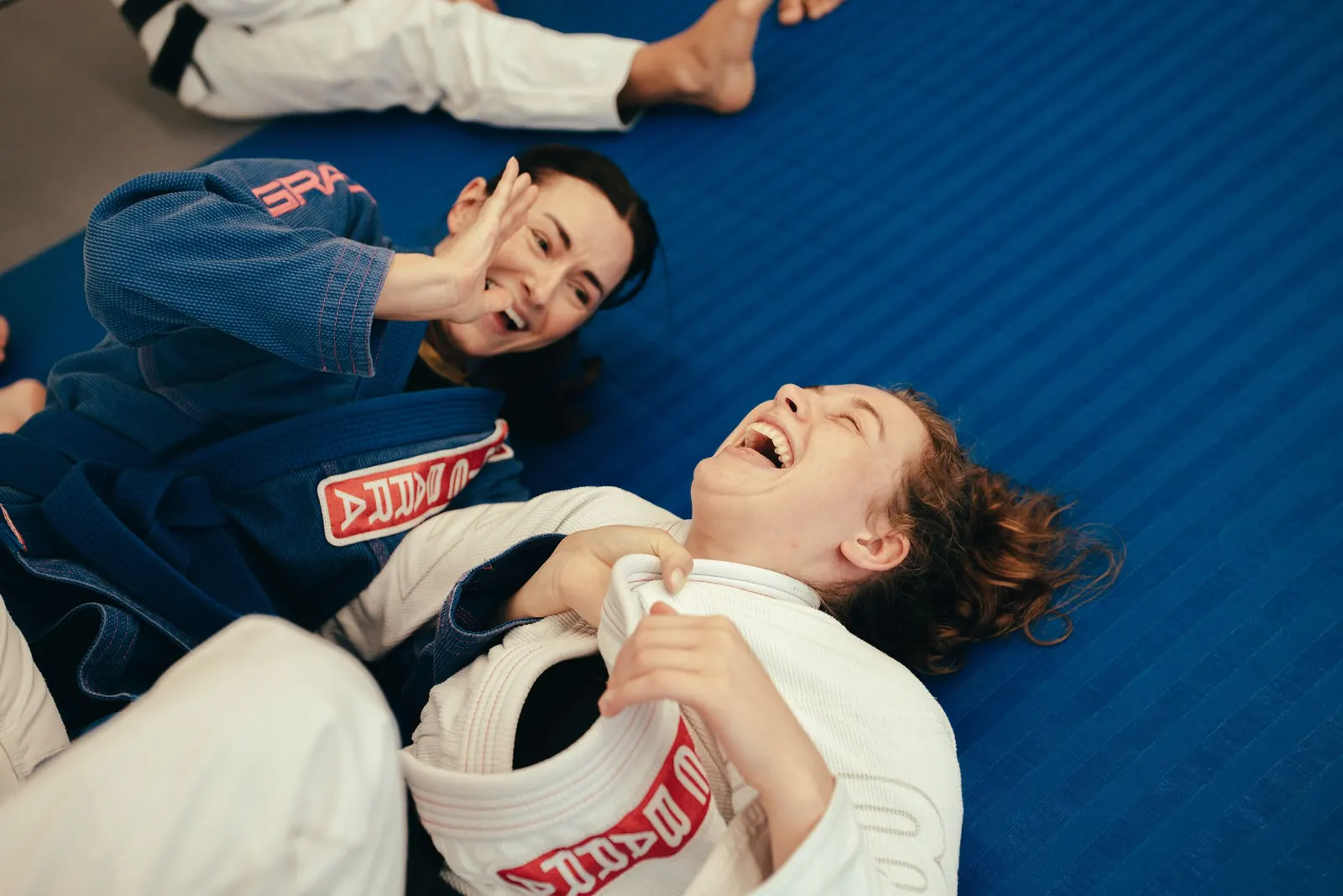 Two adult students laughing together during a roll on the mats