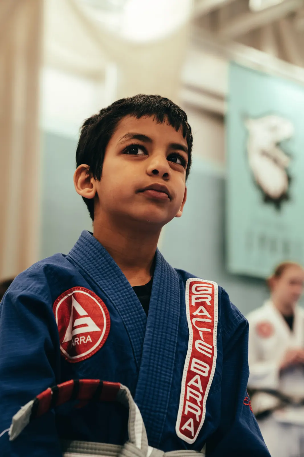 A child in a blue Gracie Barra gi looking up at a coach