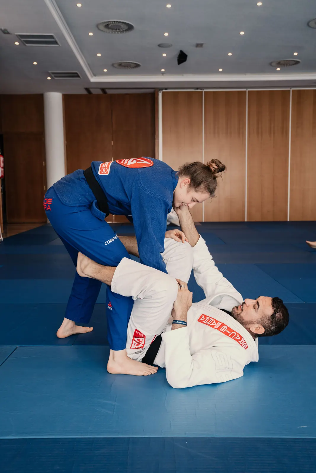 A woman in a blue gi working on guard passing with a training partner