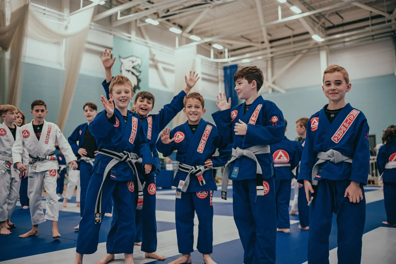 Young students in blue gis smiling and waving after training