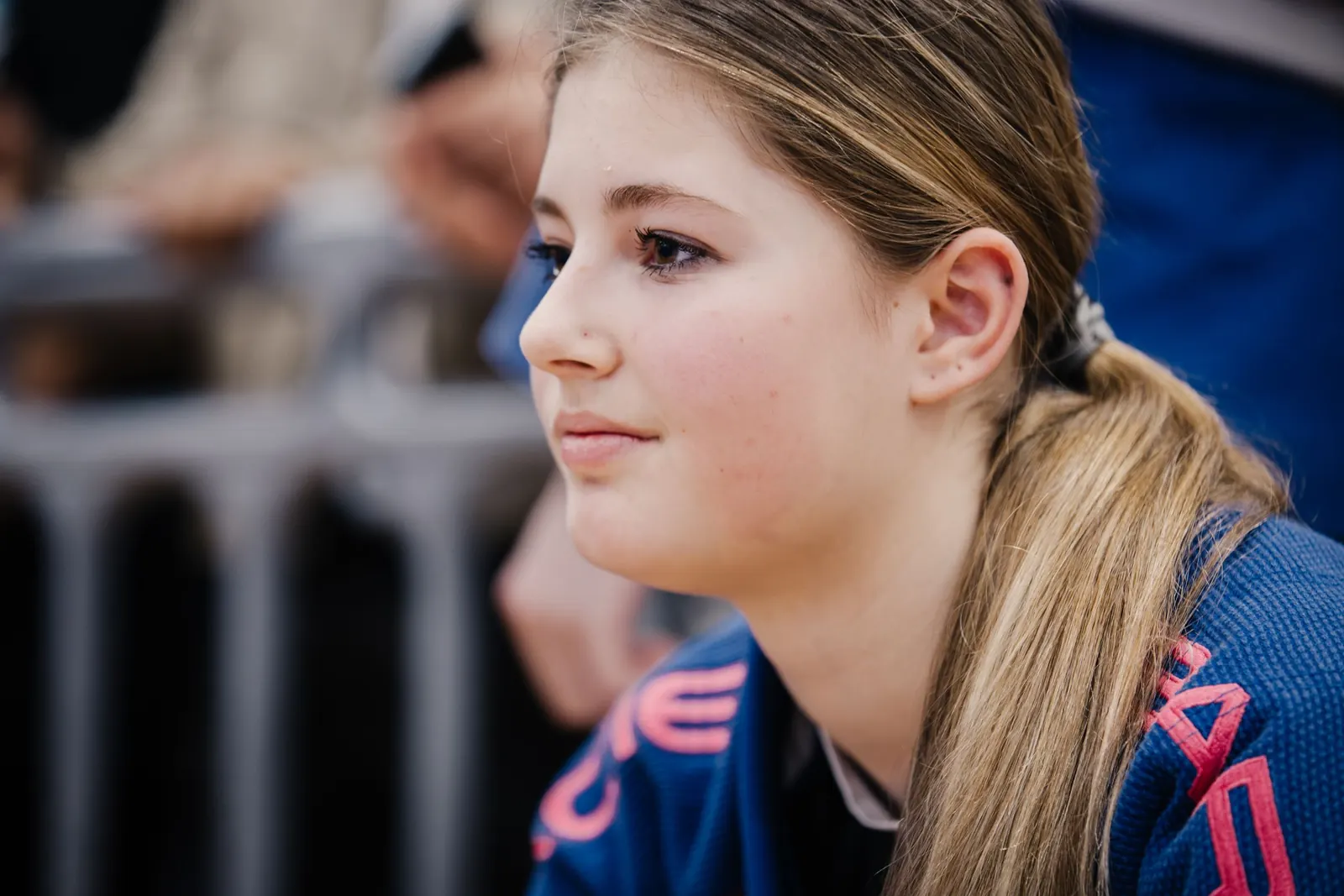 A teenage student in a blue gi watching from the edge of the mat