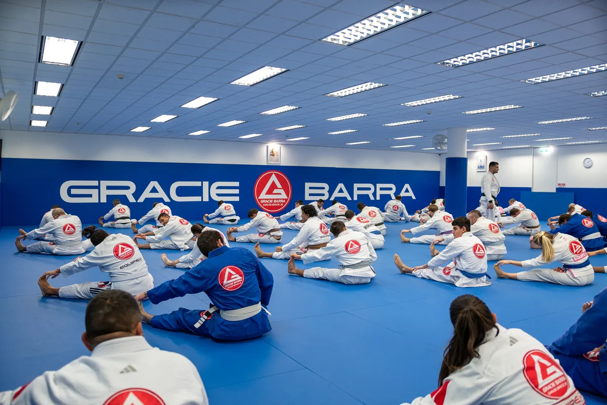 A large Gracie Barra Jiu-Jitsu session stretching on the mats